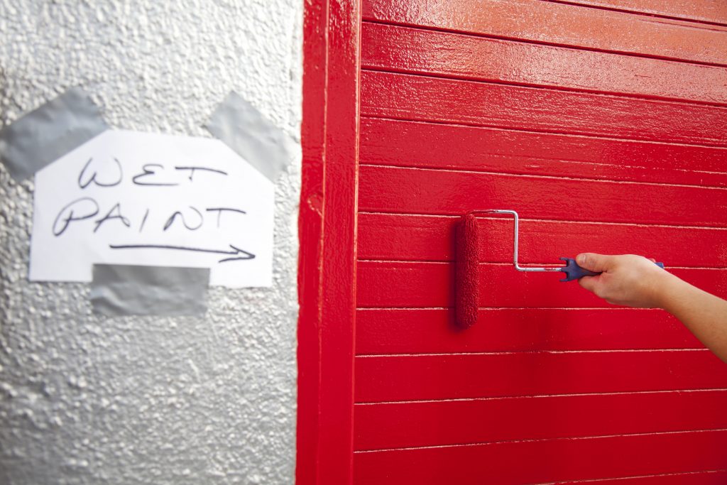 Wet paint sign next to a door beiing painted red with a roller