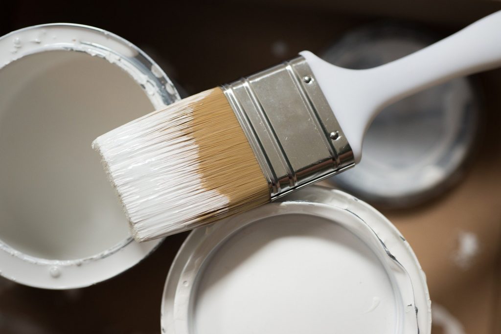 Paint brush on top of tins of white paint for disposal 
