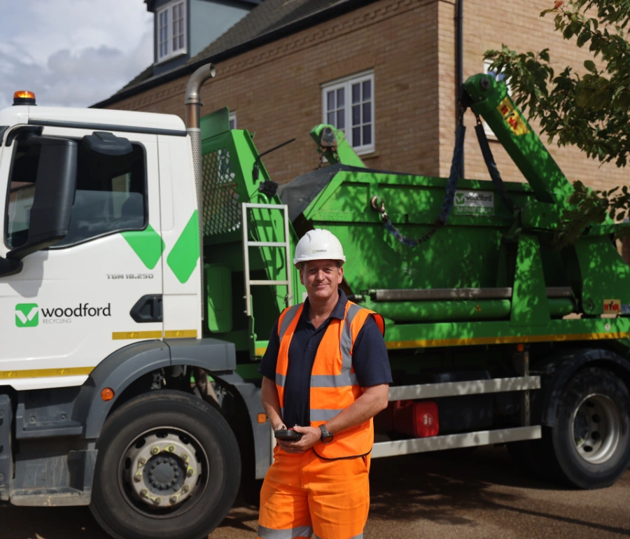 Worker standing beside Woodford Recycling skip hire vehicle